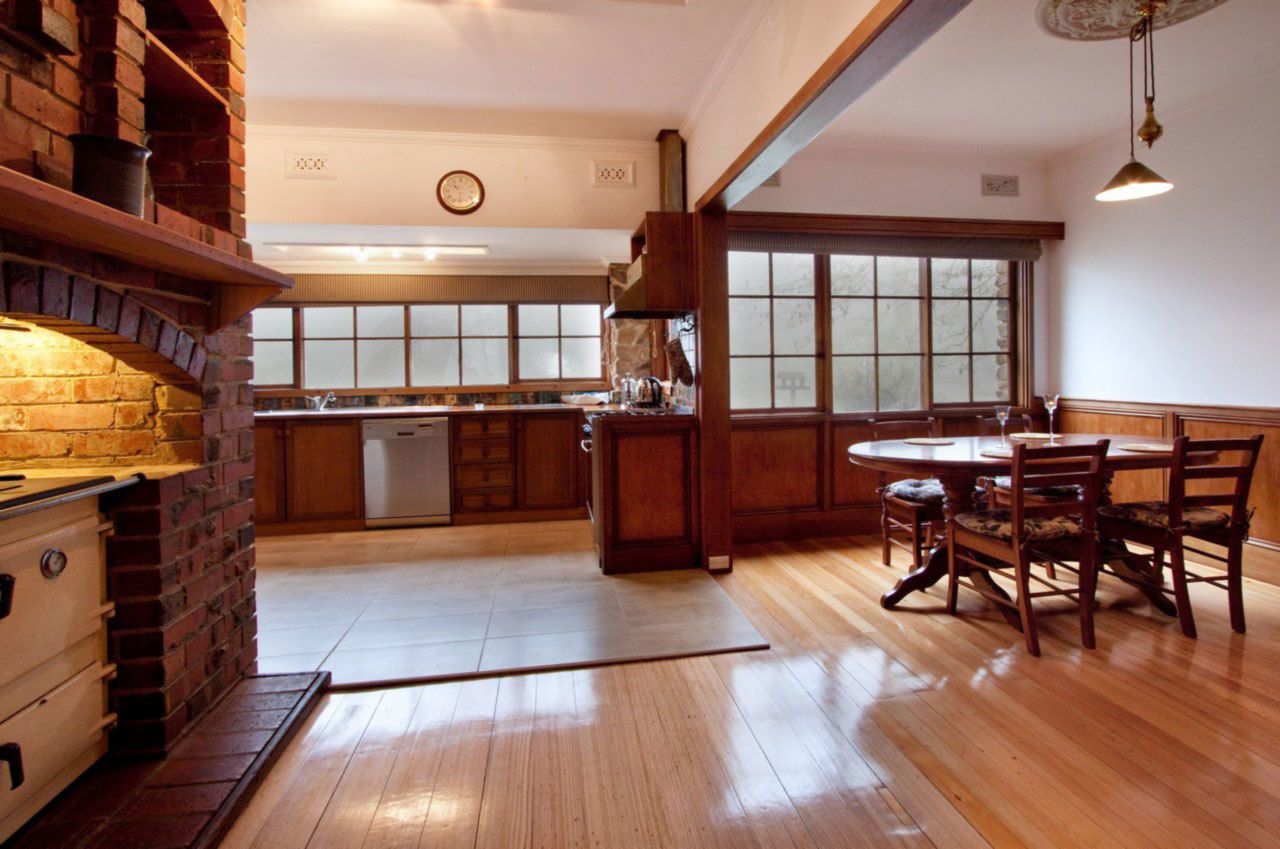 A spacious kitchen with wooden cabinets, a brick oven, and a dining area with wooden chairs and a table.