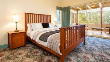 Quarto com cama de madeira, mesa de cabeceira, janela com cortinas e varanda com vista para árvores.
