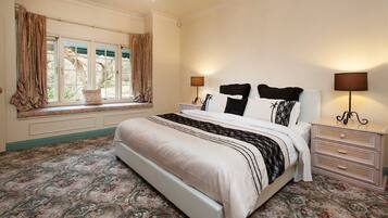 A bedroom with a large bed, two bedside tables, a window with curtains, and a patterned carpet.