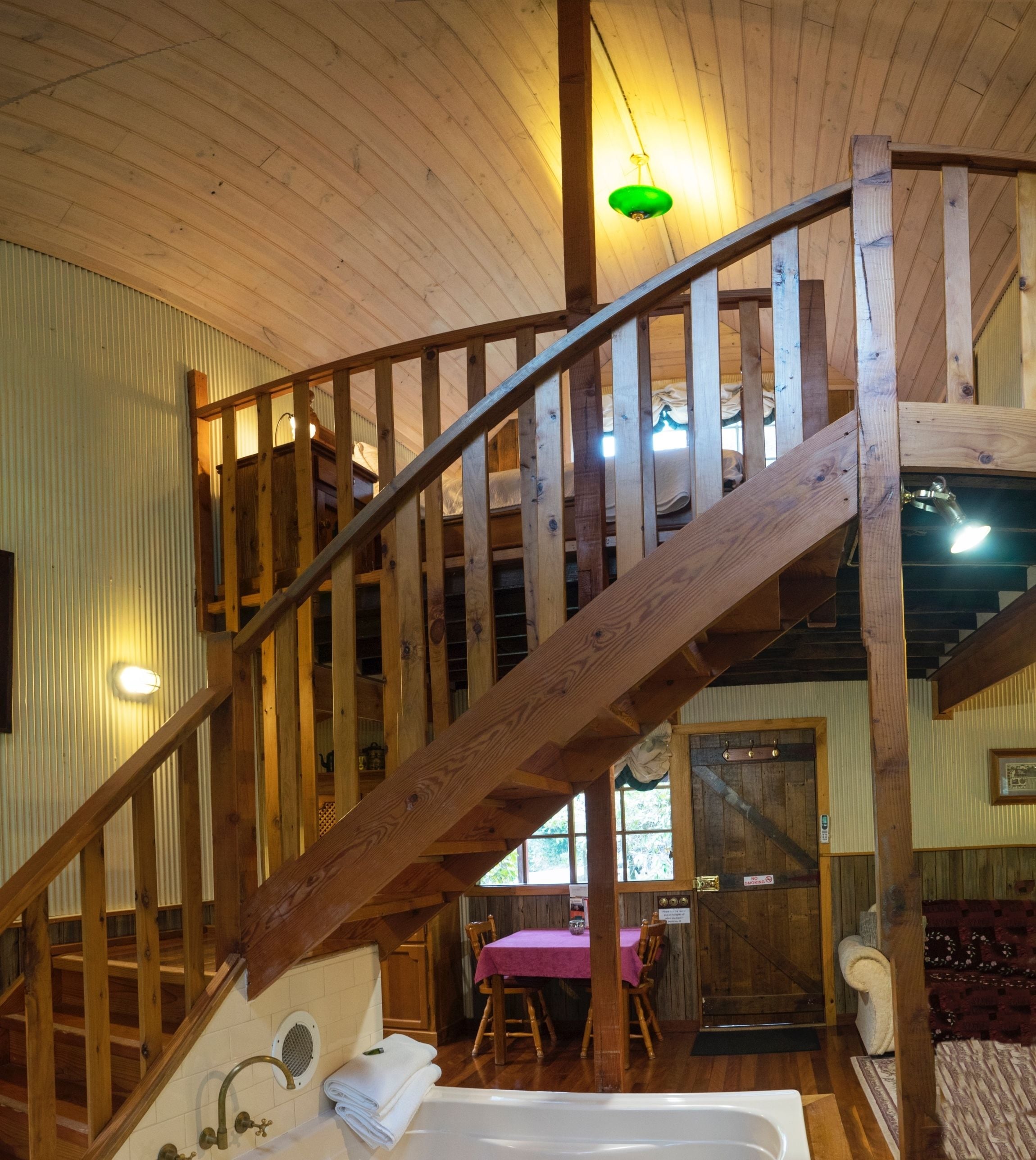 Uma escada de madeira leva a um andar superior, um banheiro com banheira e uma sala de jantar com mesa e cadeiras.