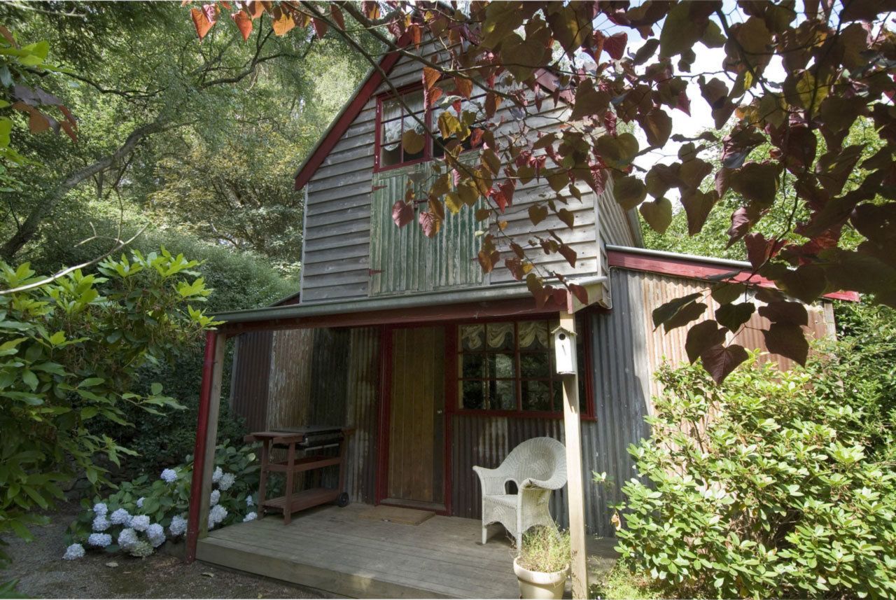 A rustic wooden cabin with a porch, surrounded by lush greenery and hydrangeas.