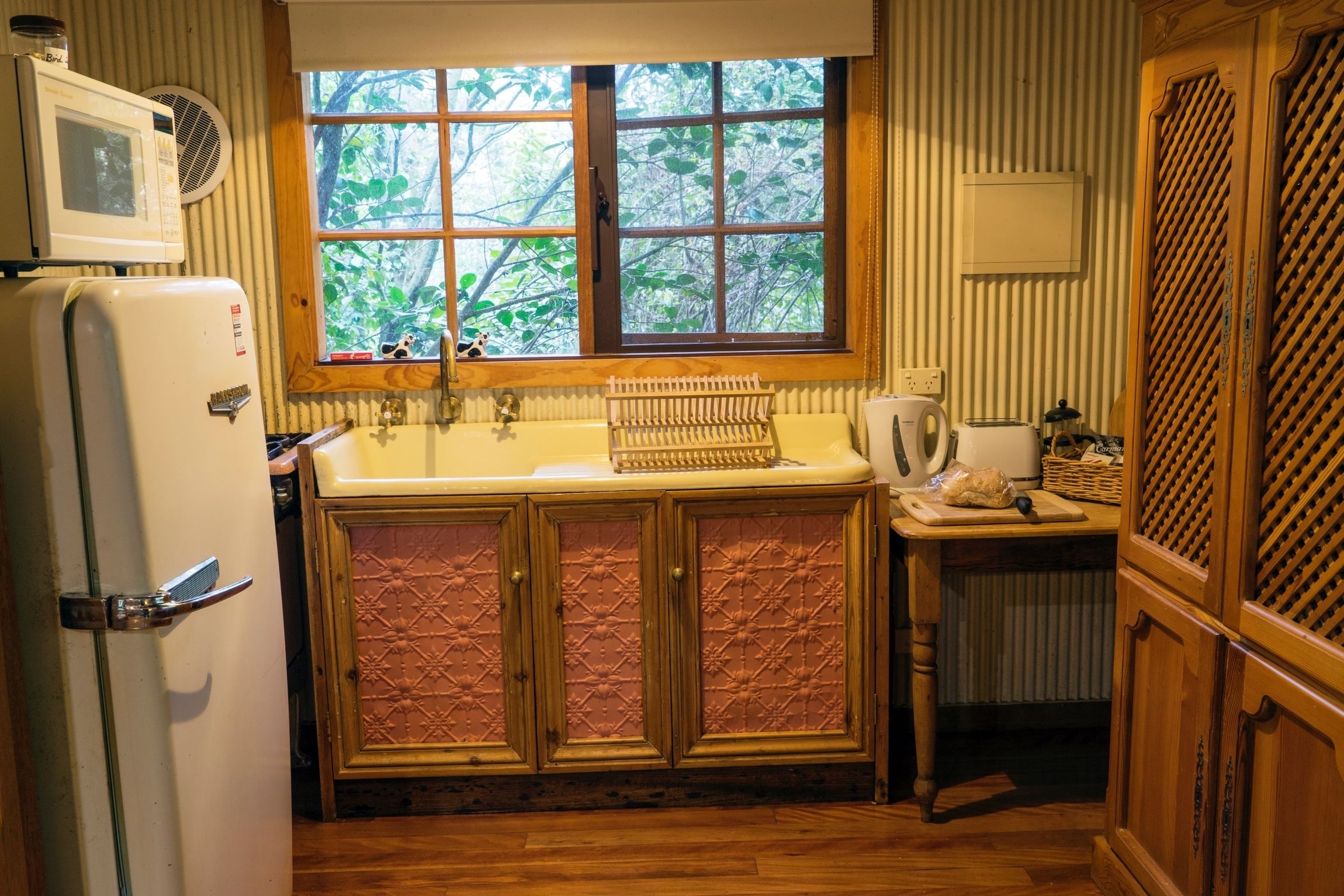A compact kitchen with a window, wooden cabinets, a refrigerator, and a sink.