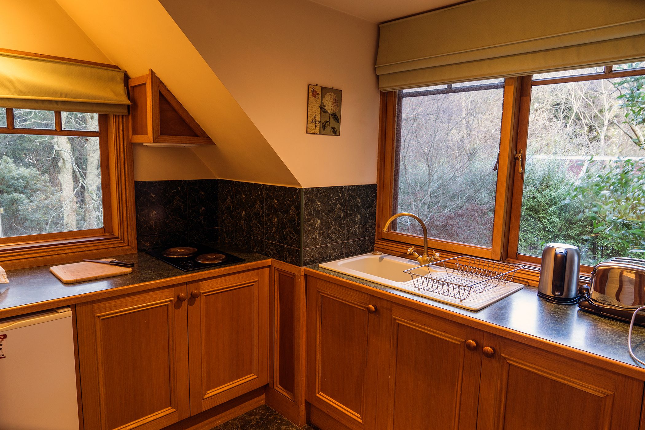 Una cocina con armarios de madera, un lavamanos, una ventana con vista a árboles y una estufa.