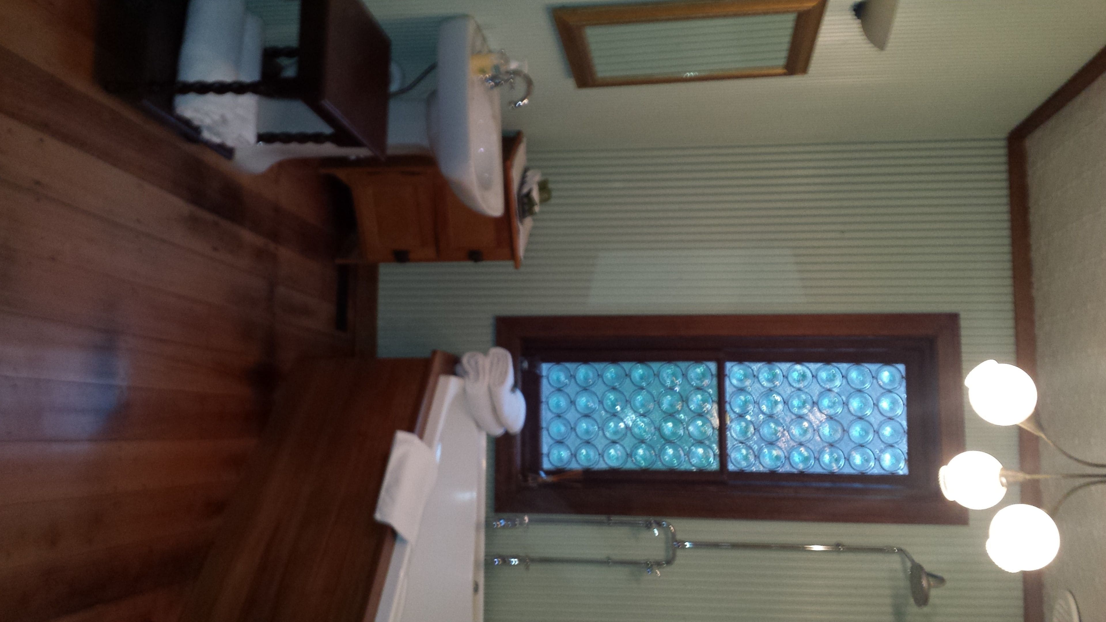 A bathroom with wooden flooring, a sink, a mirror, a towel rack, and a window with a frosted glass design.