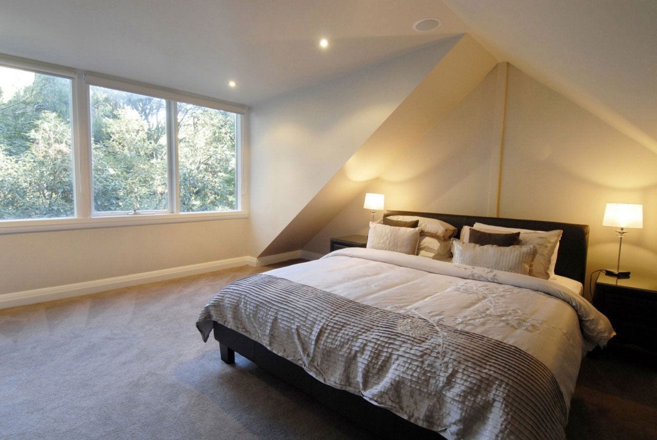 A bedroom with a large bed, two bedside lamps, and a window with a view of trees.