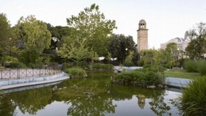 Un étang paisible, avec un clocher en arrière-plan, entouré d’une végétation luxuriante et bordé d’une allée pavée.