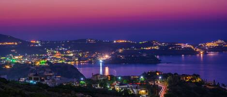 A coastal town at dusk with illuminated buildings and a winding road.