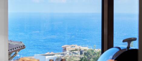 Una cocina con vistas al mar, dos lámparas colgantes de cobre y un plato de comida sobre la encimera.