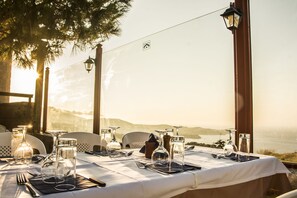 A table set for dining with a view of the sea and hills, outdoor lighting, and a clear sky.