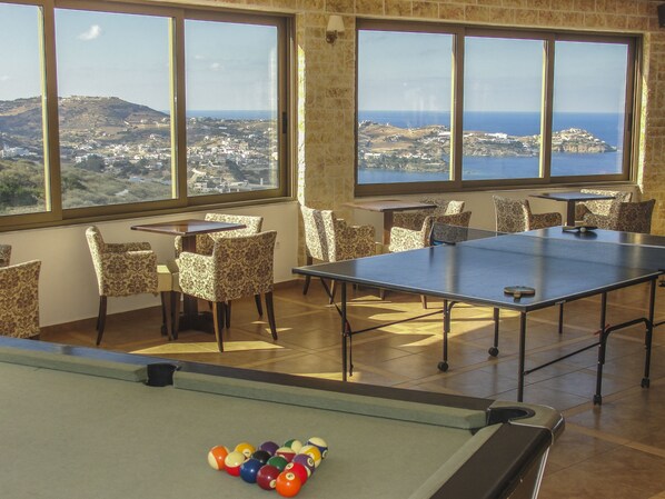 A pool table with a view of a coastal town through large windows.