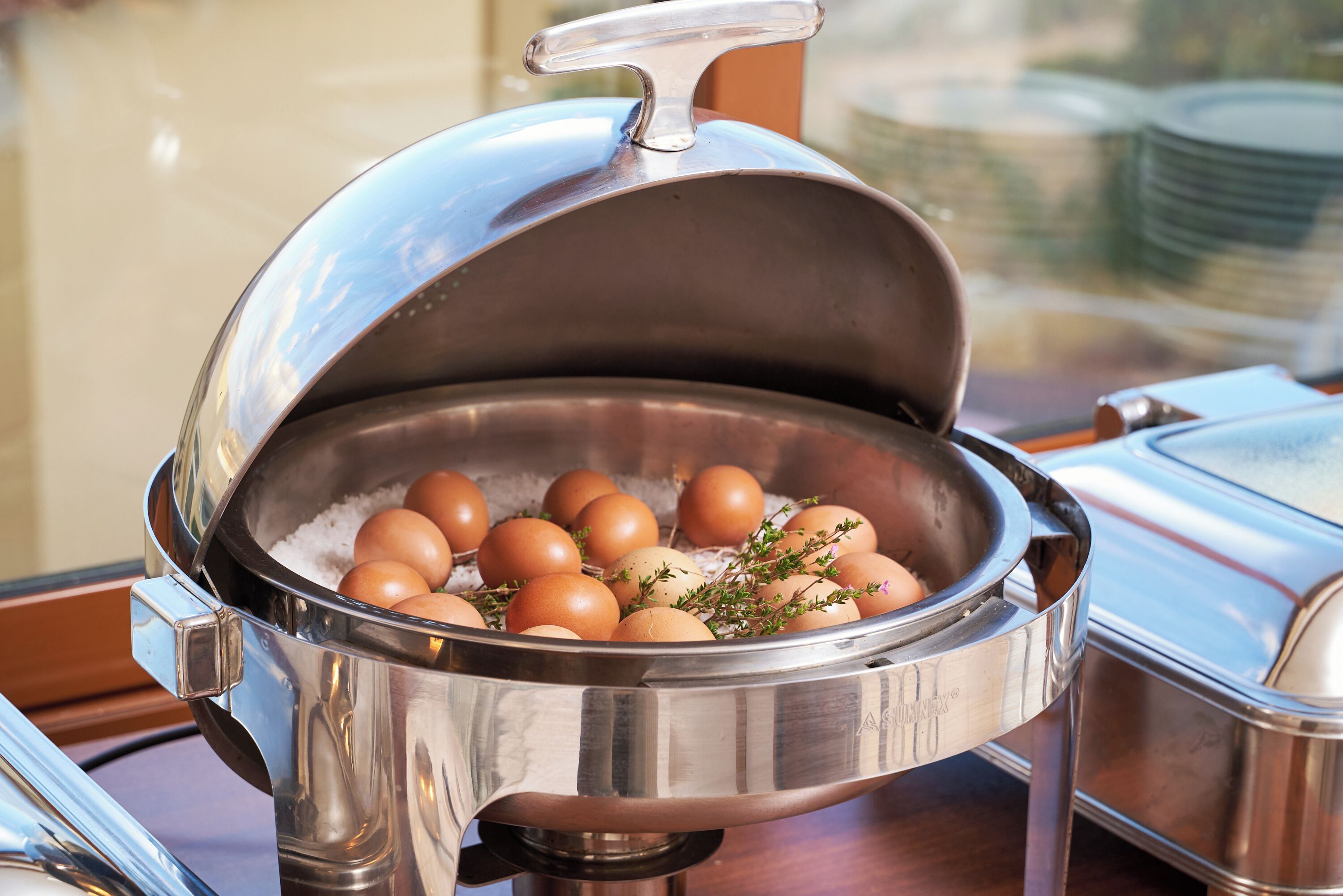 A buffet setup with a covered container holding eggs and herbs.