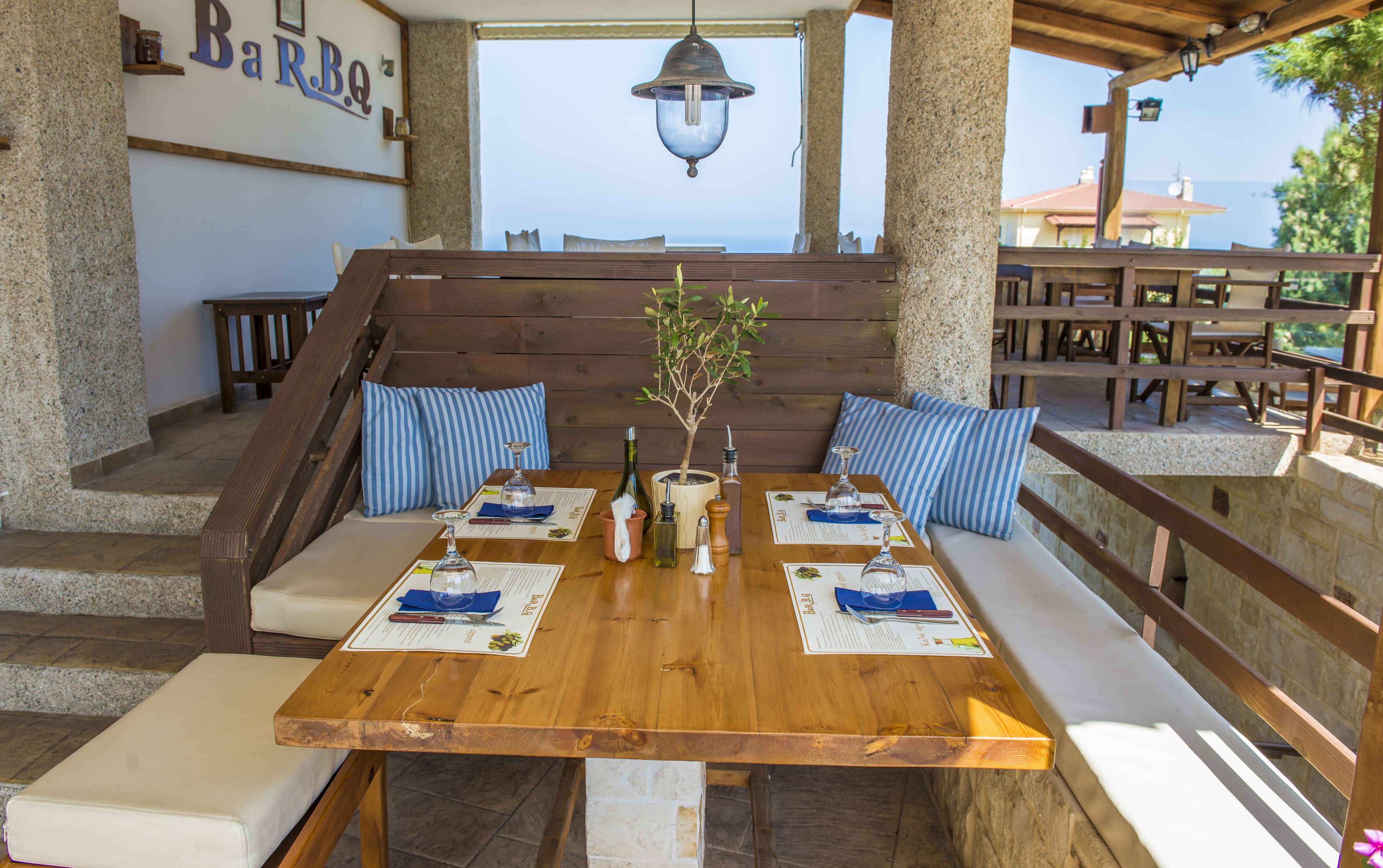 A wooden table set for dining with blue-striped cushions, a small potted plant, and various bottles and glasses.