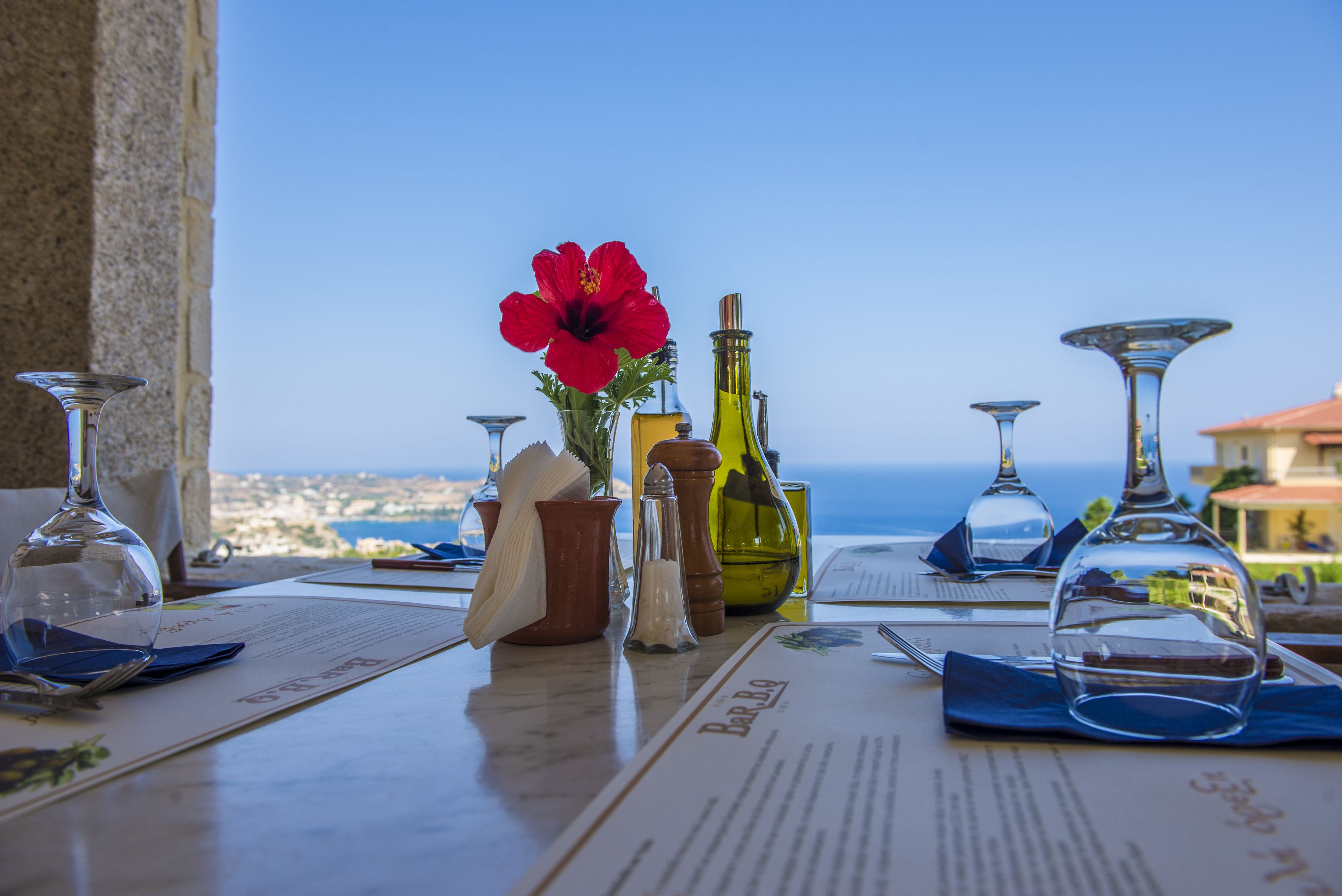 Une table dressée pour le dîner, avec un menu, des verres à vin et un arrangement floral en guise de centre de table.