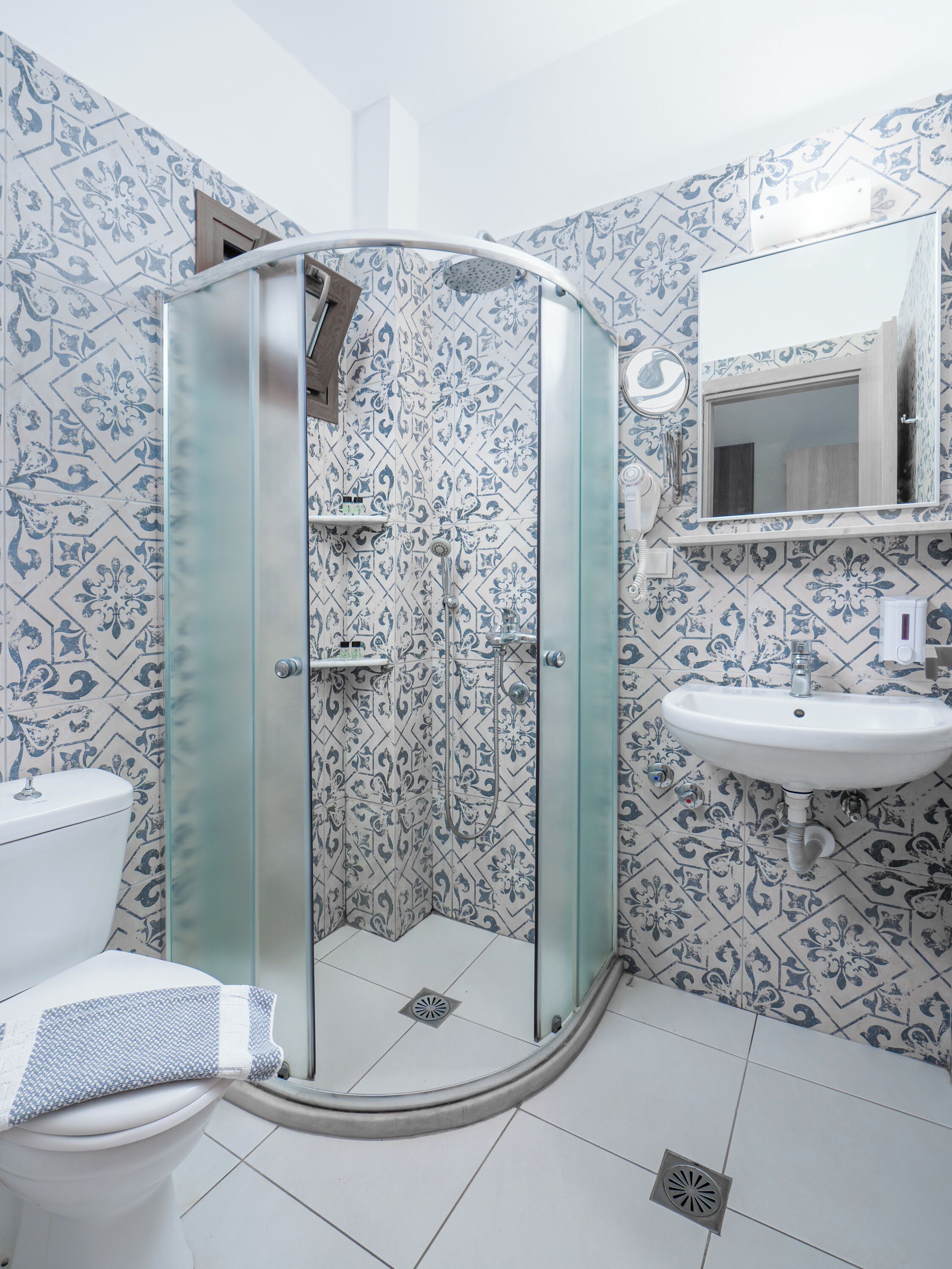 A bathroom with a glass-enclosed shower, a white sink, and patterned tiles.