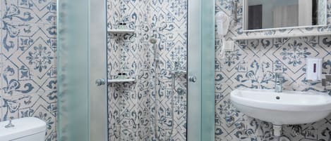 A bathroom with a glass-enclosed shower, a white sink, and patterned tiles.