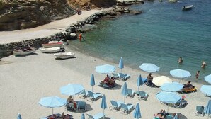 A beach with clear blue water, rocky cliffs, and several sun loungers and umbrellas. - Spiros-Soula Family Hotel & Apartments (Malevizi)