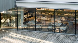 Un restaurante moderno con fachada de vidrio, terraza de madera y zona de estar al aire libre.