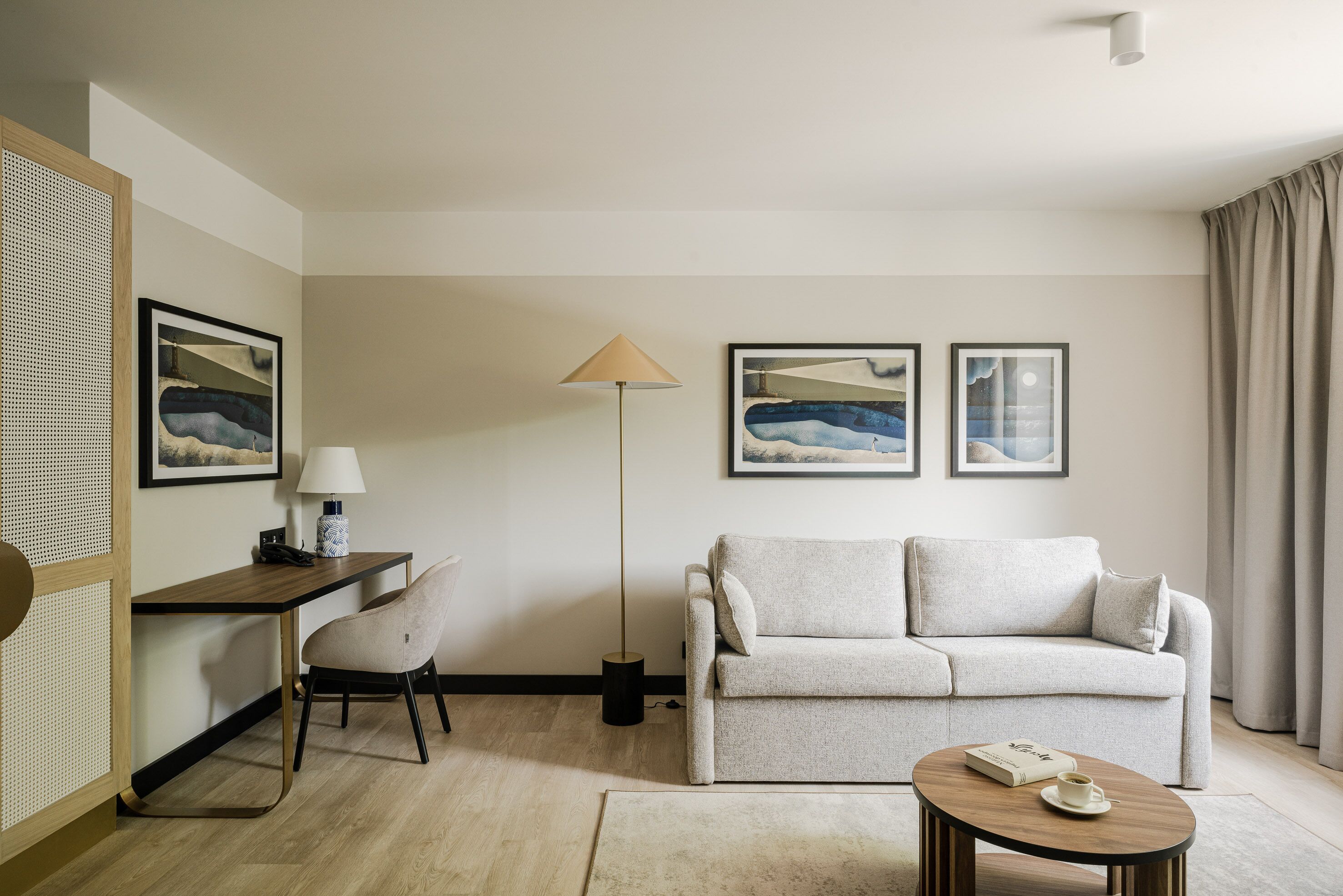A modern living room with a sofa, a desk, a chair, a lamp, and artwork on the walls.