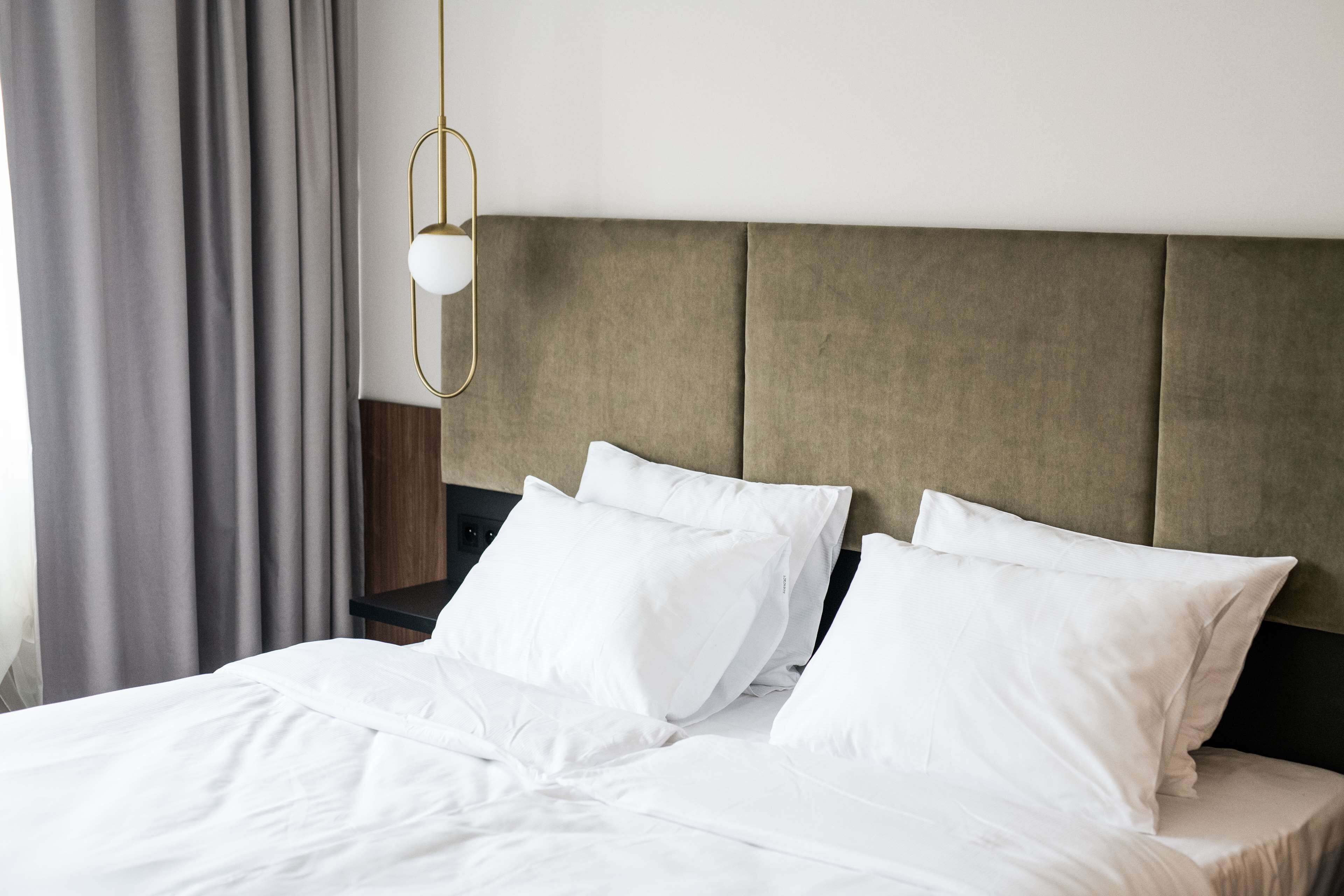 Una cama bien hecha con sábanas y almohadas blancas, una mesita de noche de madera y una lámpara colgante.