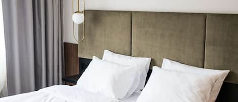 Una cama bien hecha con sábanas y almohadas blancas, una mesita de noche de madera y una lámpara colgante.