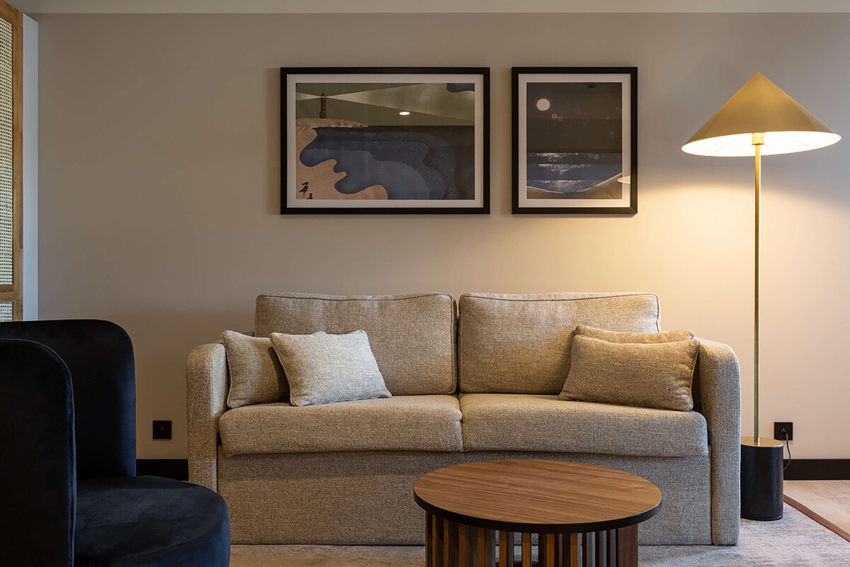 Un salon moderne avec un canapé, une table basse ronde et deux œuvres d’art encadrées accrochées au mur.