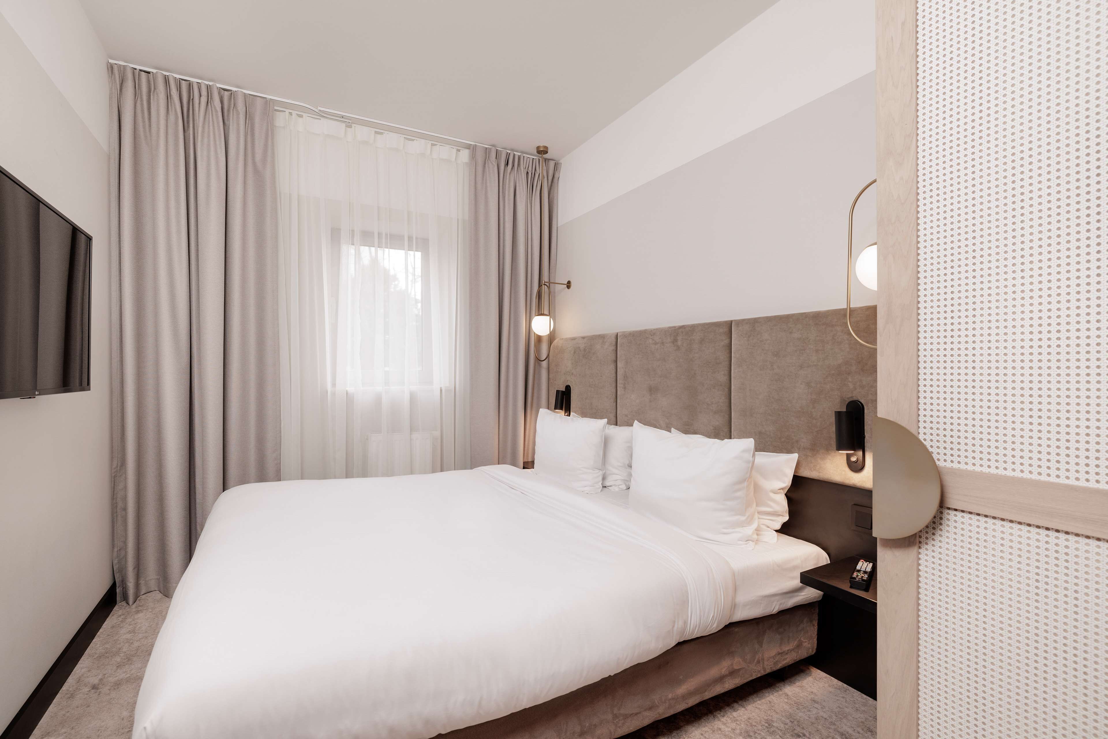 A neatly arranged hotel room with a large bed, a bedside table, and a wall-mounted light fixture.