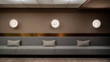 A modern waiting area with a grey sofa, striped pillows, and three wall-mounted lamps.