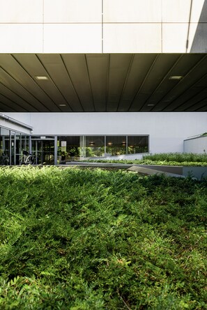 Un edificio moderno con entrada de vidrio, un aparcamiento para bicicletas y un jardín en la azotea.