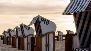 Una hilera de cabañas de playa con números, marcos de madera y toldos a rayas.