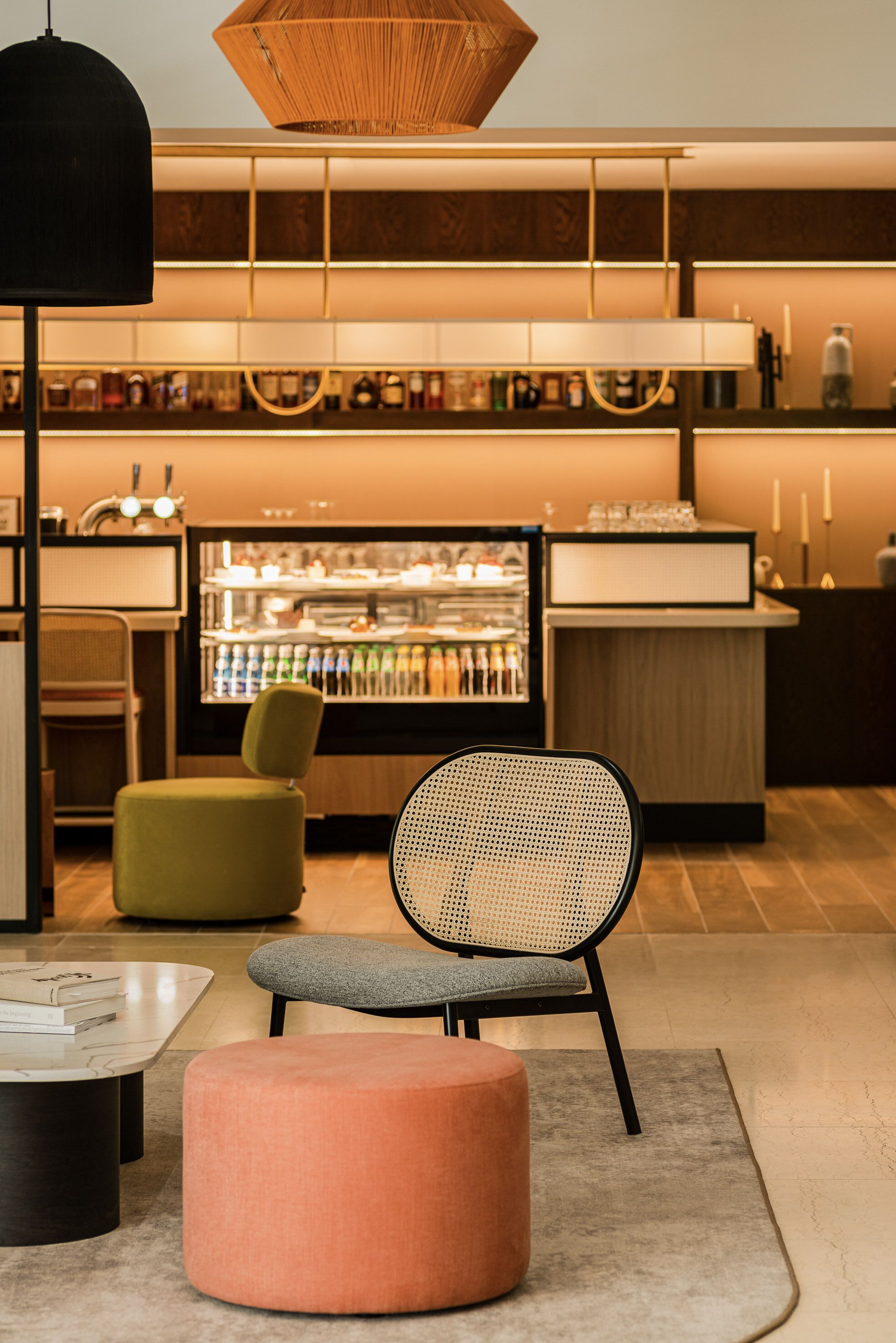 Eine moderne Bar mit Sitzgelegenheiten, einem mit Getränken gefüllten Kühlschrank und einer warmen, einladenden Beleuchtung.