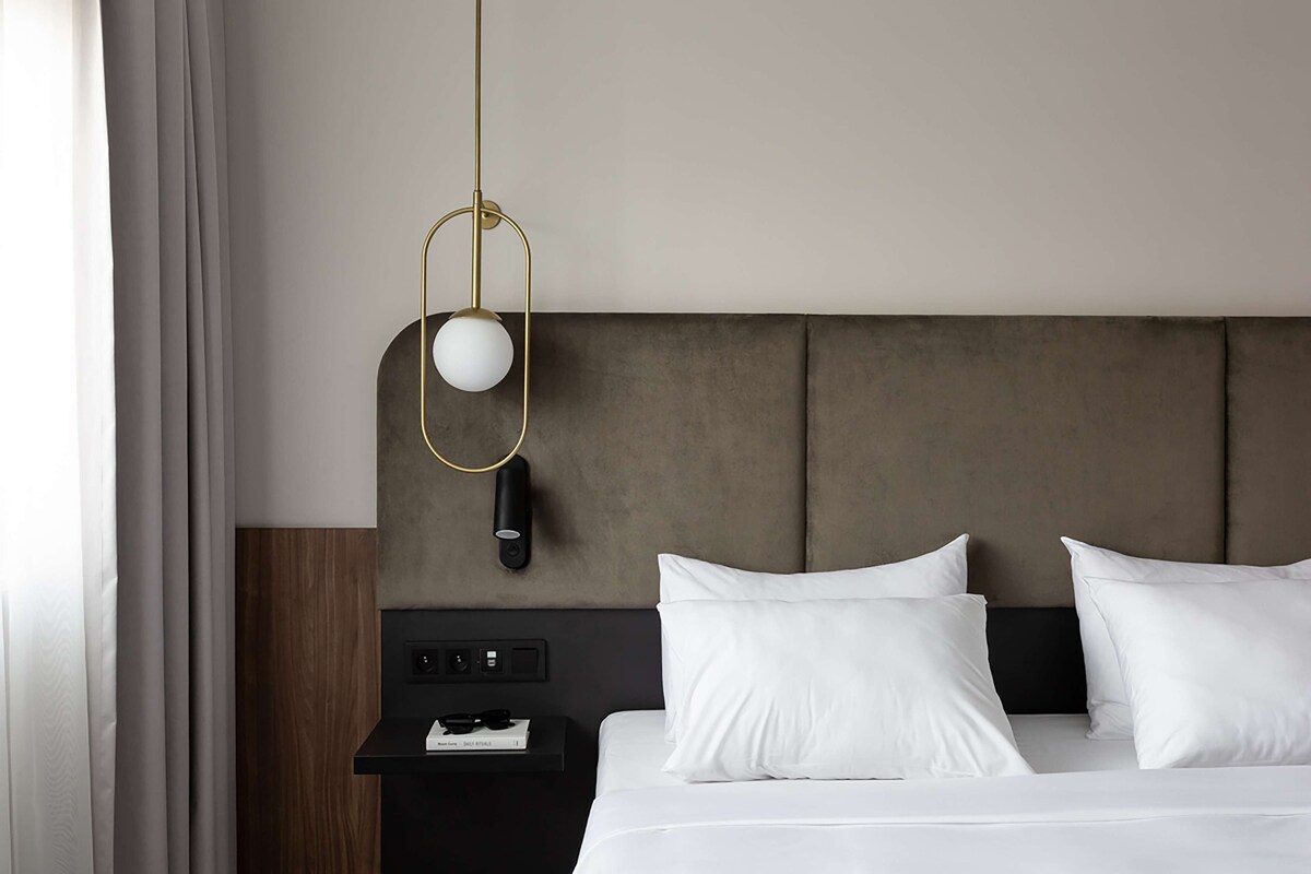 Une chambre d’hôtel moderne avec un grand lit, une table de chevet avec une lampe et une vue sur la ville.