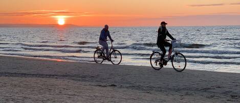 A beach with two cyclists riding along the shore during sunset.