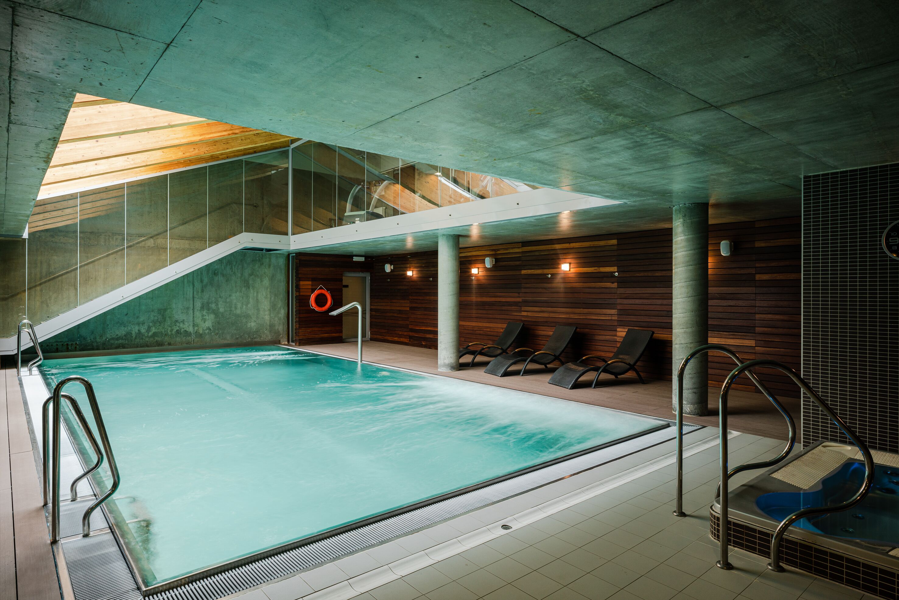 An indoor swimming pool with a glass ceiling, wooden panel walls, and a hot tub area.