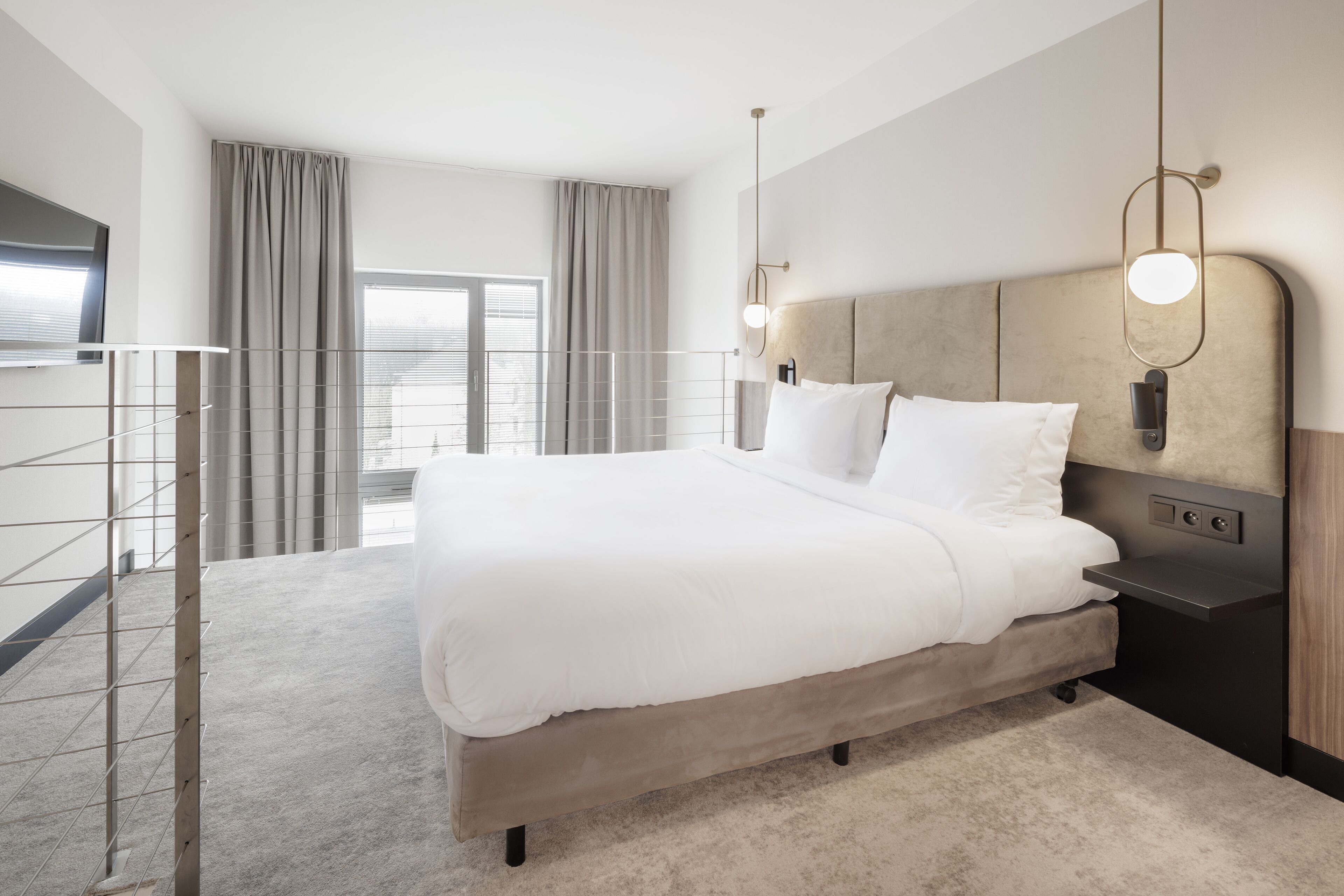 A modern hotel room with a large bed, a nightstand, a wall-mounted light, and a balcony with curtains.