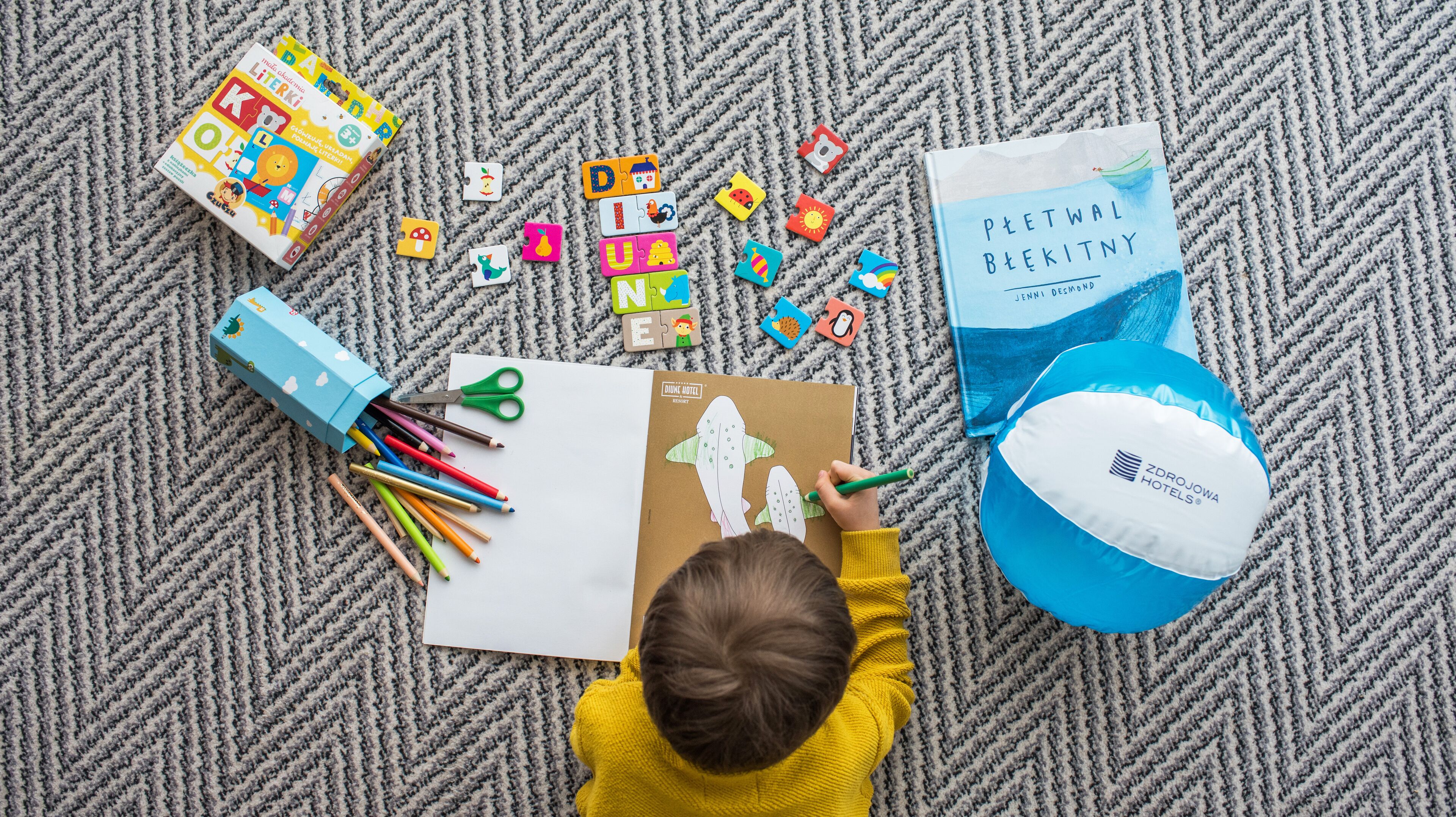 A child drawing on a paper with colored pencils and a blue box nearby.