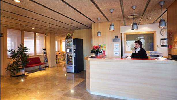 Zona de recepción de un hotel con un mostrador de madera, un reloj y una máquina expendedora.