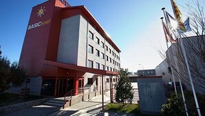 Un edificio con fachada roja y blanca, un letrero que dice "BASIChotel" y un asta con varias banderas.
