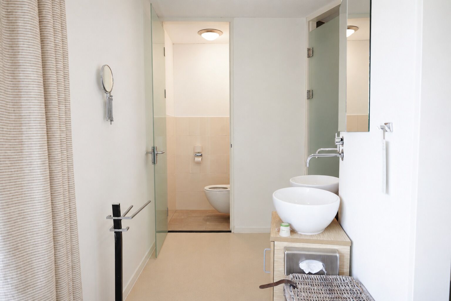 A modern bathroom with a glass shower enclosure, a toilet, and two white sinks.
