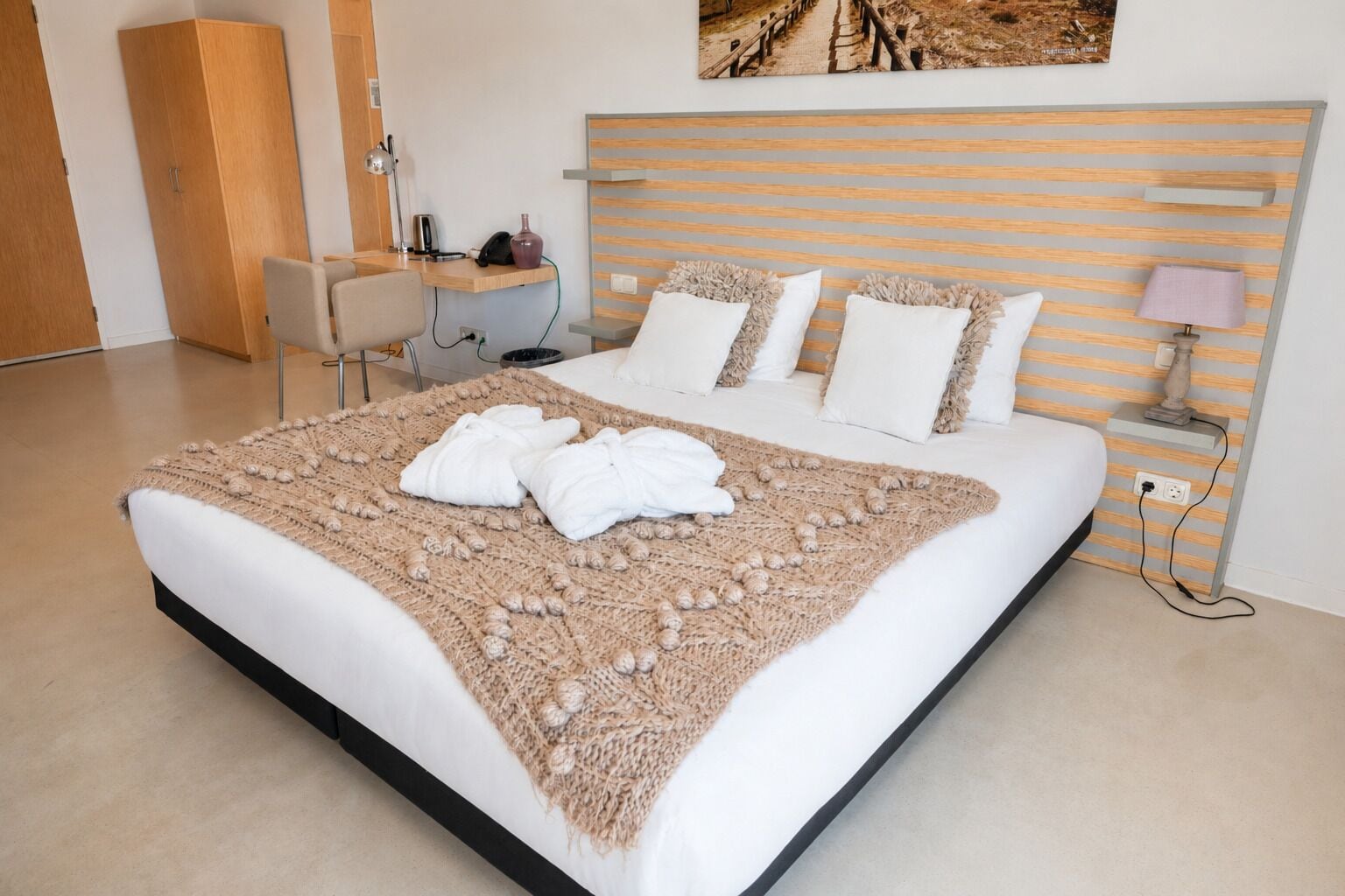 Una habitación de hotel con una cama, un escritorio, una silla y una mesita de noche con lámpara.