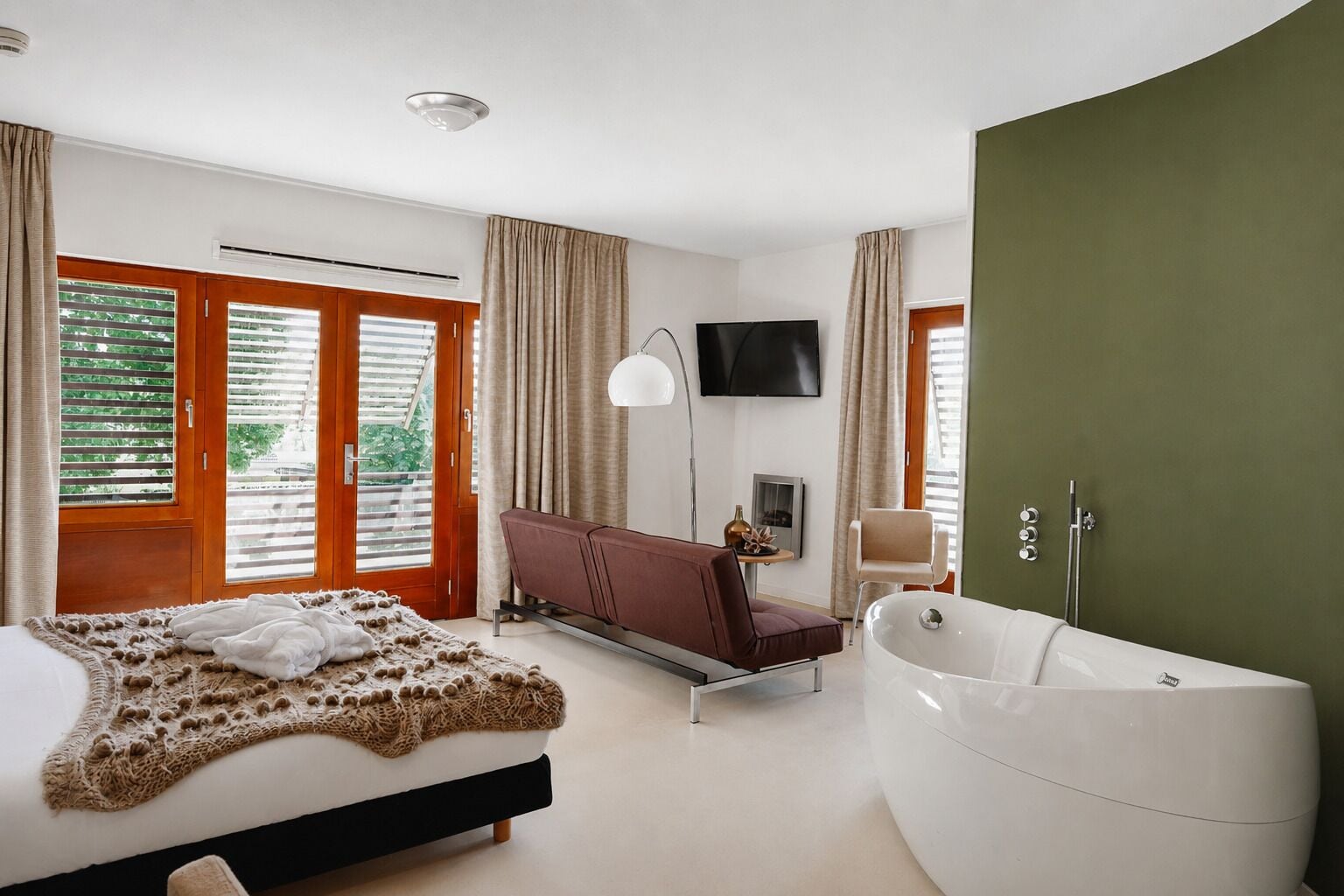 Een moderne slaapkamer met een groot bed, een bank, een televisie en een bad.
