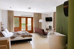 A modern hotel room with a bed, a sofa, a large bathtub, a TV, and a balcony with curtains. - Boshotel Overberg (Overberg)