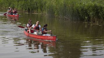Un grupo de personas en un canoa roja navegando por un río tranquilo bordeado de abundante vegetación.