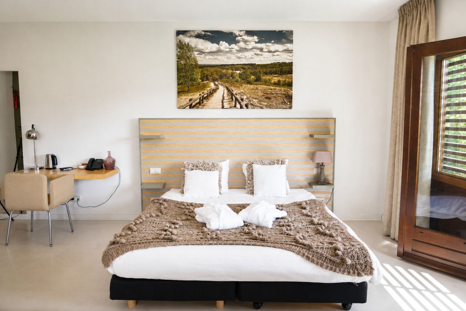 A modern hotel room with a bed, a desk, and a window.