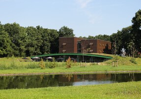 Um edifício moderno com telhado verde e uma ponte sobre um lago.