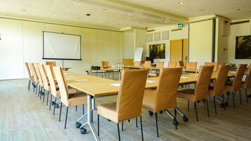 Un salón de conferencias con una pantalla grande, varias mesas y sillas.