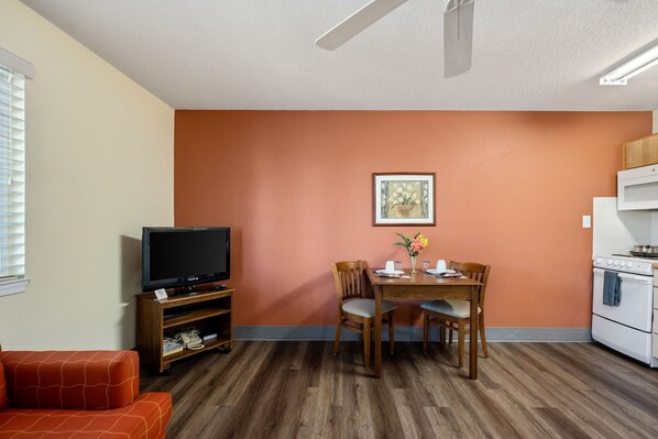 Un espacio habitable compacto con televisión, mesa de comedor, sillas y kitchenette.