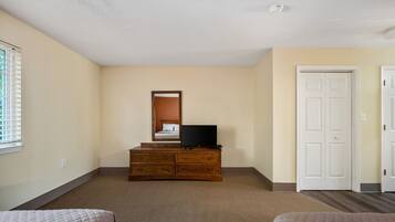 A bedroom with a wooden dresser, a television, a bed, and a white door.