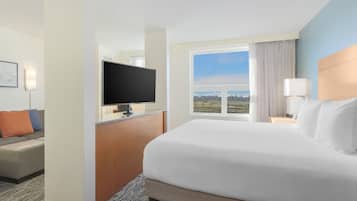 A hotel room with a large bed, a flat-screen TV, a desk with a lamp, and a view of the outdoors.
