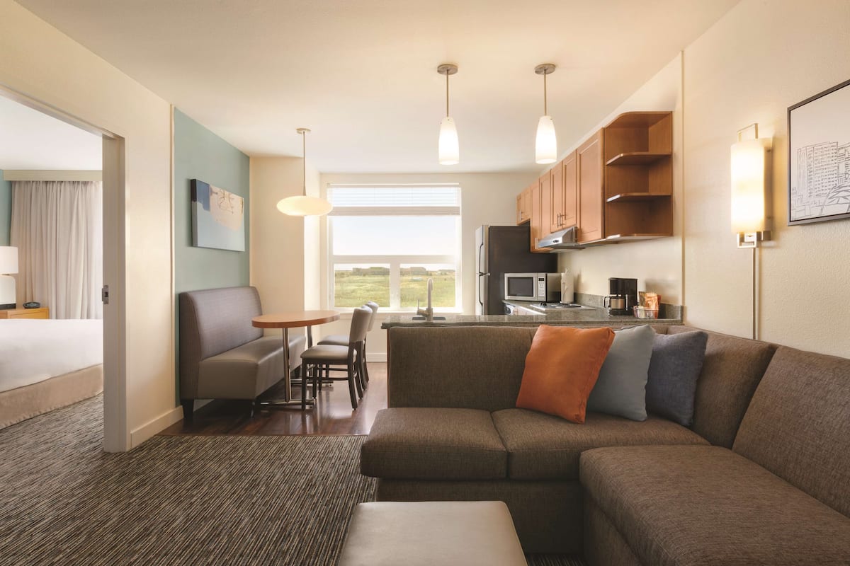 A modern hotel room with a living area, kitchenette, and a large window offering a view.