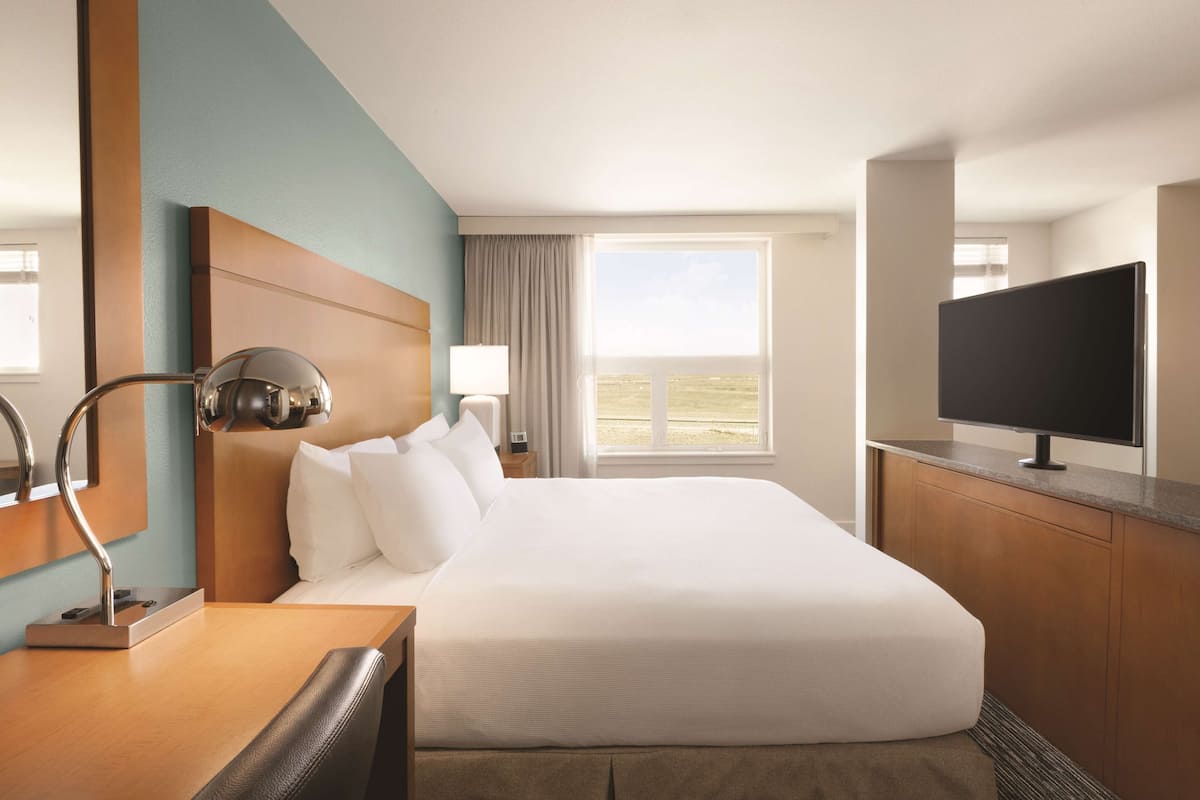 A hotel room with a large bed, a desk with a lamp, a television, and a window with a view.